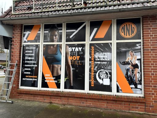 Fensterfront eines Fitnessstudios mit Bildern von Sportlern und Werbetexten.