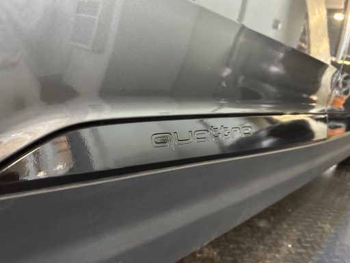 Glänzender, silberner Seitenbereich eines Fahrzeugs mit eingeprägtem Schriftzug.