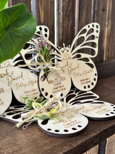 Holzschilder in Form von Schmetterlingen mit eingravierten Namen und Blumen dekoriert.