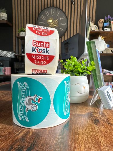 Eine Rolle mit Etiketten und eine Packung mit Aufschrift "Buch Kiosk" auf einem Tisch.