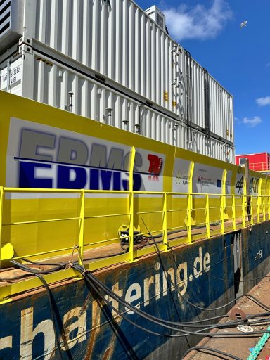 Gelbe Geländerstruktur mit Containern im Hintergrund und dem Schriftzug "CDM" darauf.
