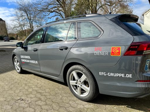 Grauer Kombi mit Aufklebern, geparkt auf einem Kiesplatz.