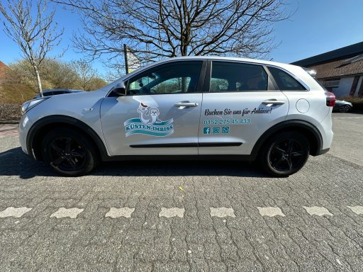 Silberner SUV mit Logo und Schriftzug auf der Seitenfläche, vor blauem Himmel.