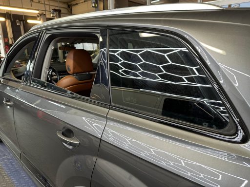 Grauer SUV mit braunem Innenraum und glänzendem Fenster, in einer Werkstatt.