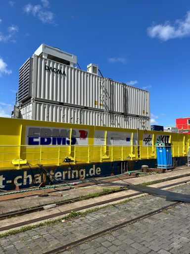 Container und Baustelle mit blauer Box vor einem klaren Himmel.