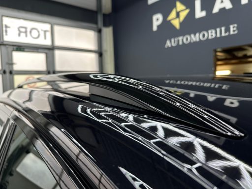 Dachspoiler eines schwarzen Autos vor einer Werkstatt mit Logo.