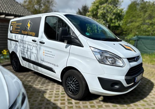 Weißer Lieferwagen mit Firmenlogo und Aufschrift auf der Seite, im Freien geparkt.