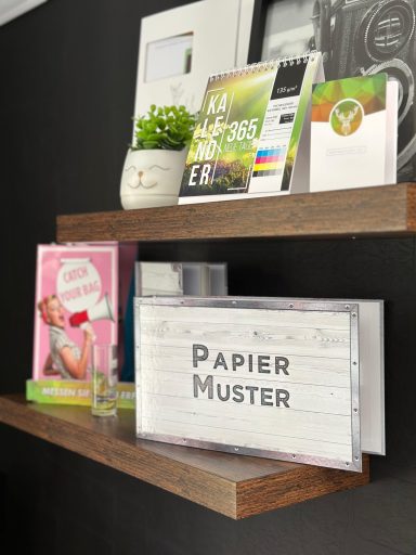 Regal mit Büchern, einem Pflanzengefäß und einem Schild mit der Aufschrift "PAPIER MUSTER".