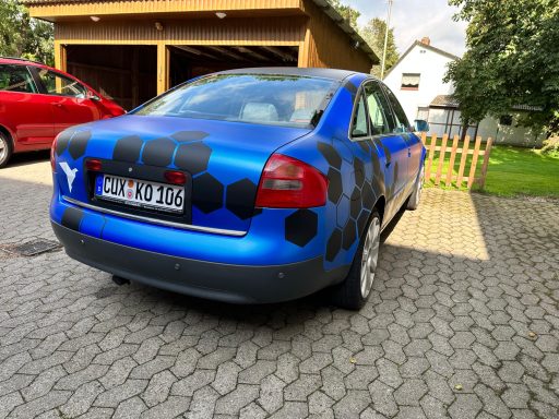 Blauer Pkw mit hexagonalem Muster in Schwarz auf der Rückseite geparkt.