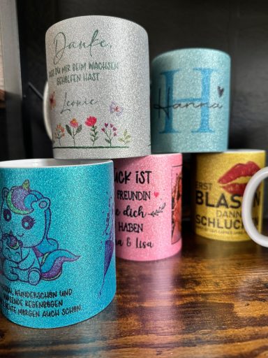 Bunte Kaffeetassen mit verschiedenen Designs und Texten auf einem Holztisch.